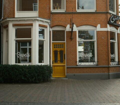 A brick building with a yellow door and windows labeled Capelli Kappers