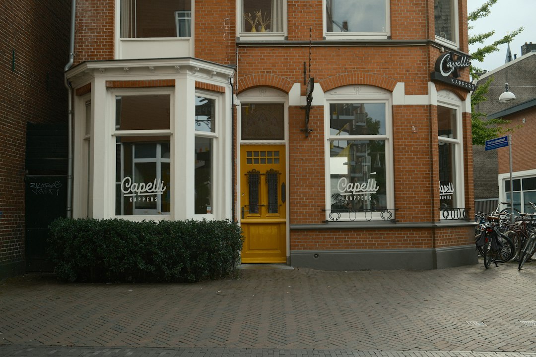 A brick building with a yellow door and windows labeled Capelli Kappers